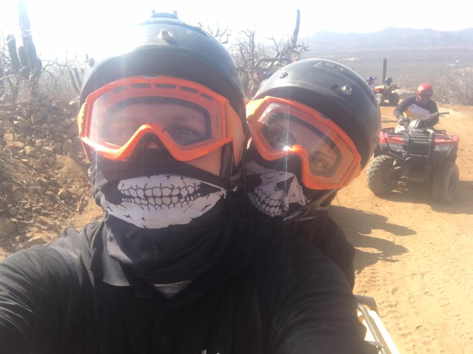 Corey and Melissa wearing helmets and goggles, smiling while sitting on an ATV during a dusty desert tour in Cabo San Lucas.