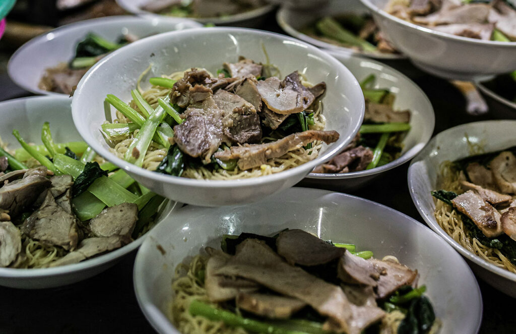 Overhead view of several bowls of Ba Mee egg noodles with roasted pork and bok choy in Bangkok's Chinatown.