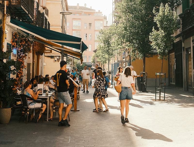 People enjoying an outdoor cafe and walking on a sunlit street in Madrid.
