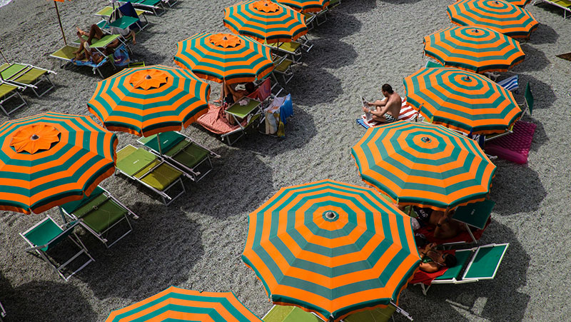 Aerial view of the Fegina beach in Monterosso al Mare, Cinque Terre, filled with colorful sun umbrellas.