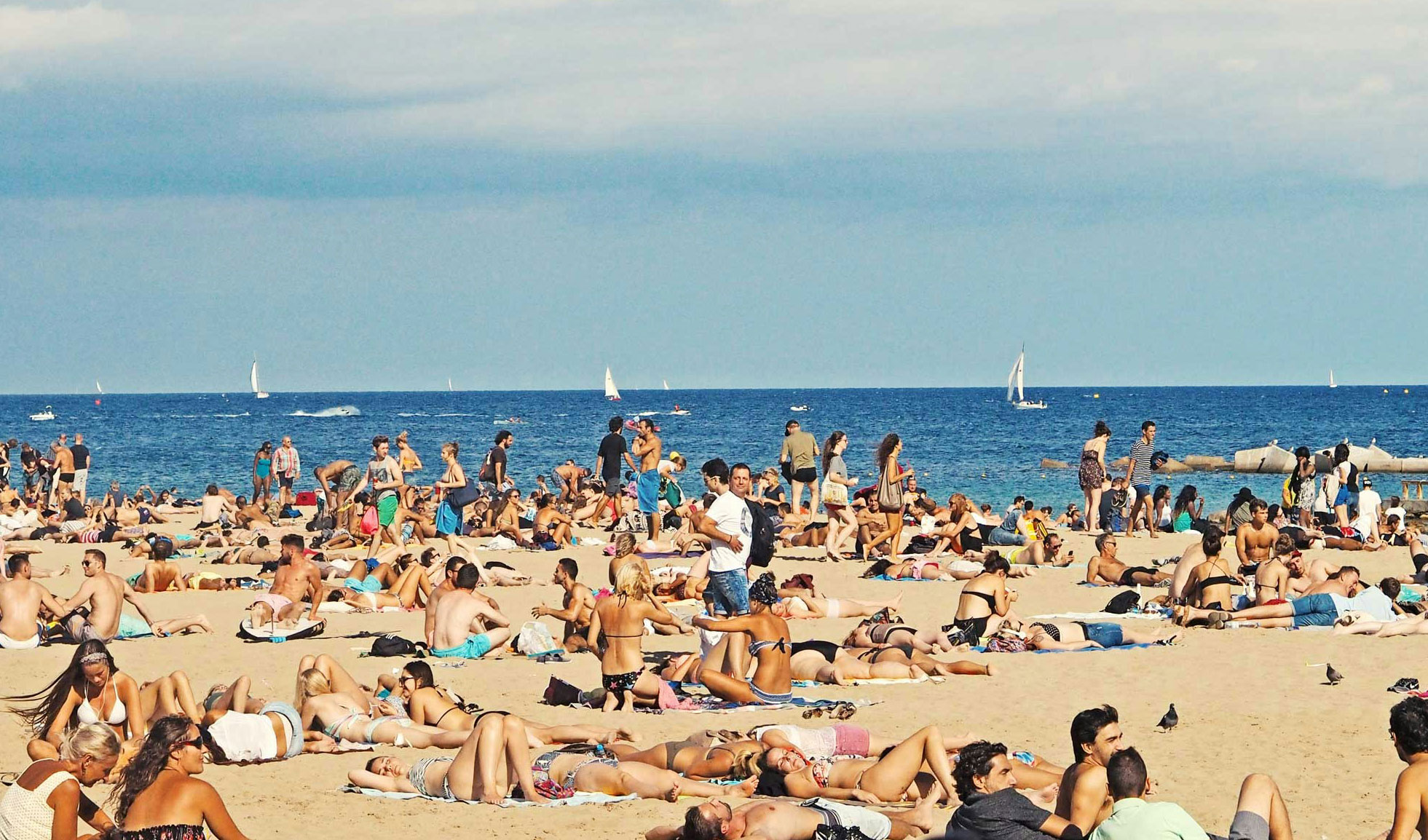 A very crowded Barcelona beach packed with people sunbathing on the sand under the sun.