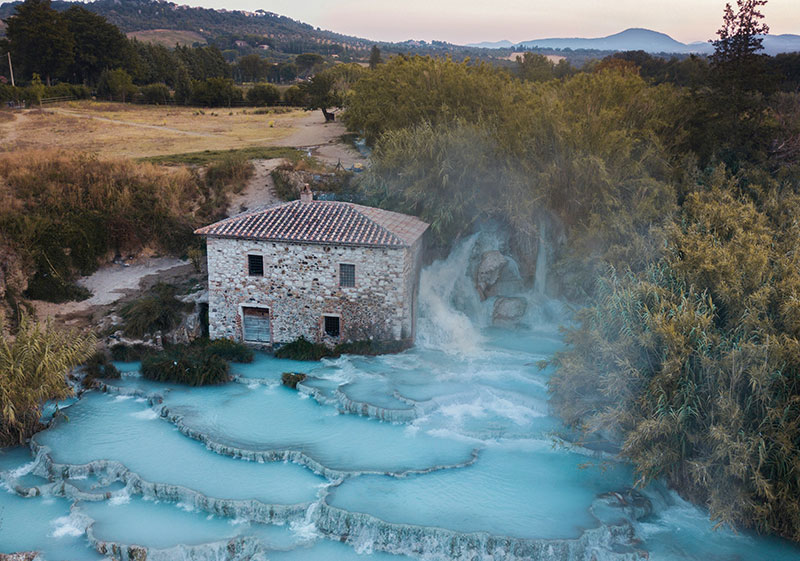 Steaming turquoise waters of the Cascate del Mulino thermal baths in Saturnia, Tuscany, with the iconic stone mill in the background.