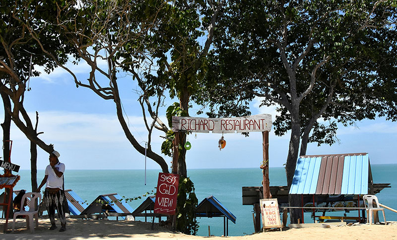 Shaded beachfront entrance with a wooden sign and view of the ocean on Koh Lanta.