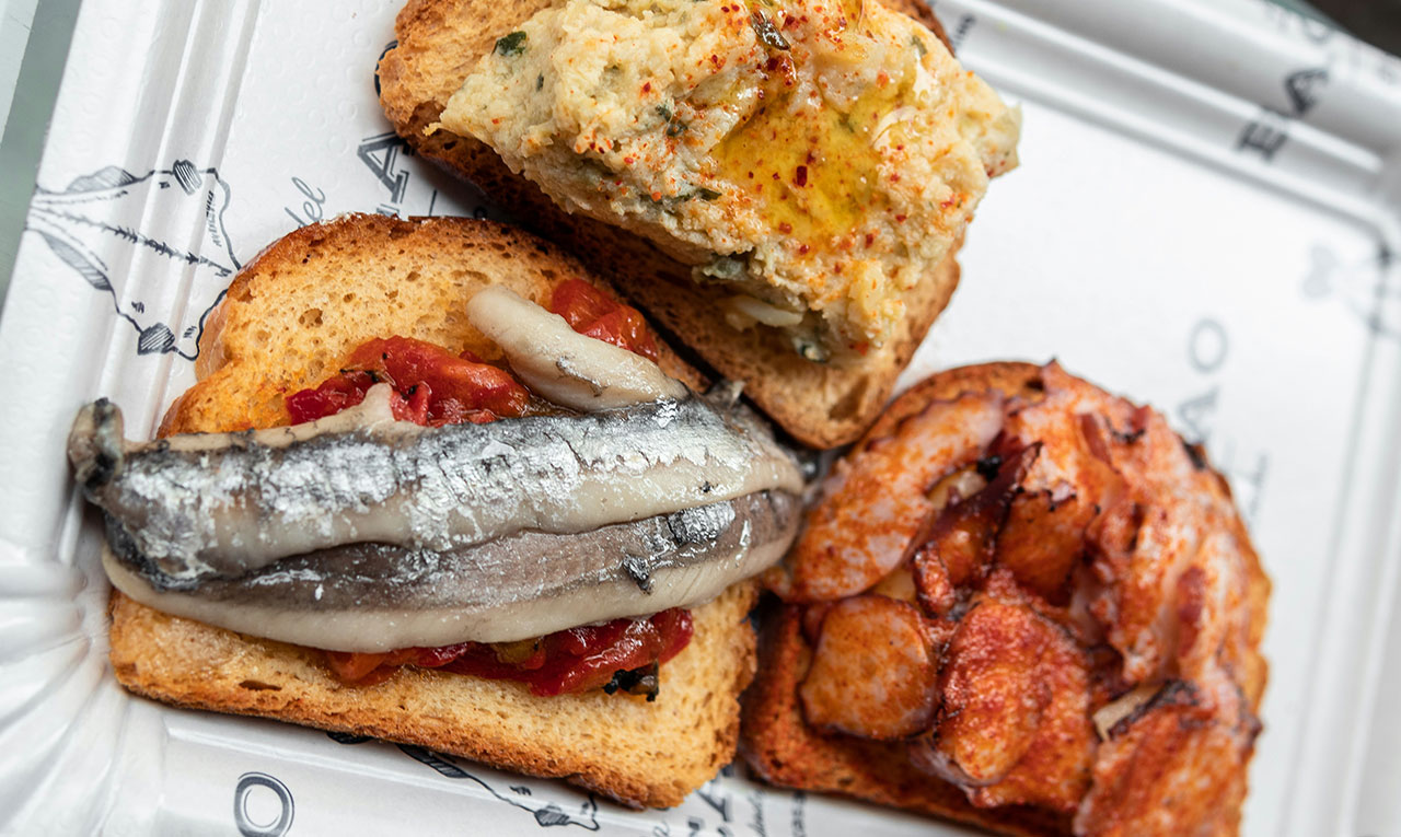 Three assorted Spanish montaditos on a plate: one with anchovies, one with shrimp, and one with fish, from Mercado de San Miguel.