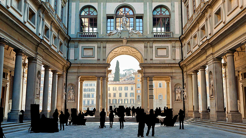 Perspective view of the Piazzale degli Uffizi courtyard in Florence, lined with Renaissance colonnades and tourists.