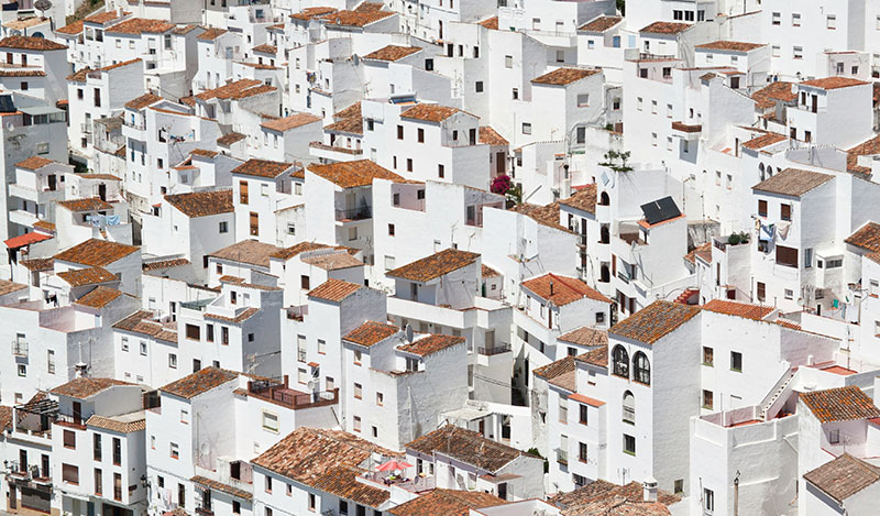 Densely packed white houses with terracotta roofs covering a hillside in Spain.