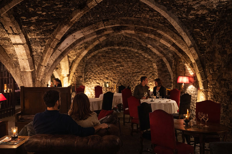 Candlelit vaulted stone wine cellar at Abbaye de Maizières hotel in Beaune, Burgundy, with guests seated at tables beneath medieval arches.