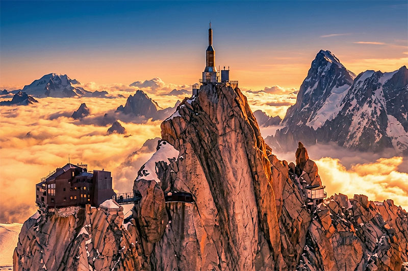 A high-resolution view of the Aiguille du Midi summit station perched on a jagged rocky peak in Chamonix, surrounded by clouds and snow.