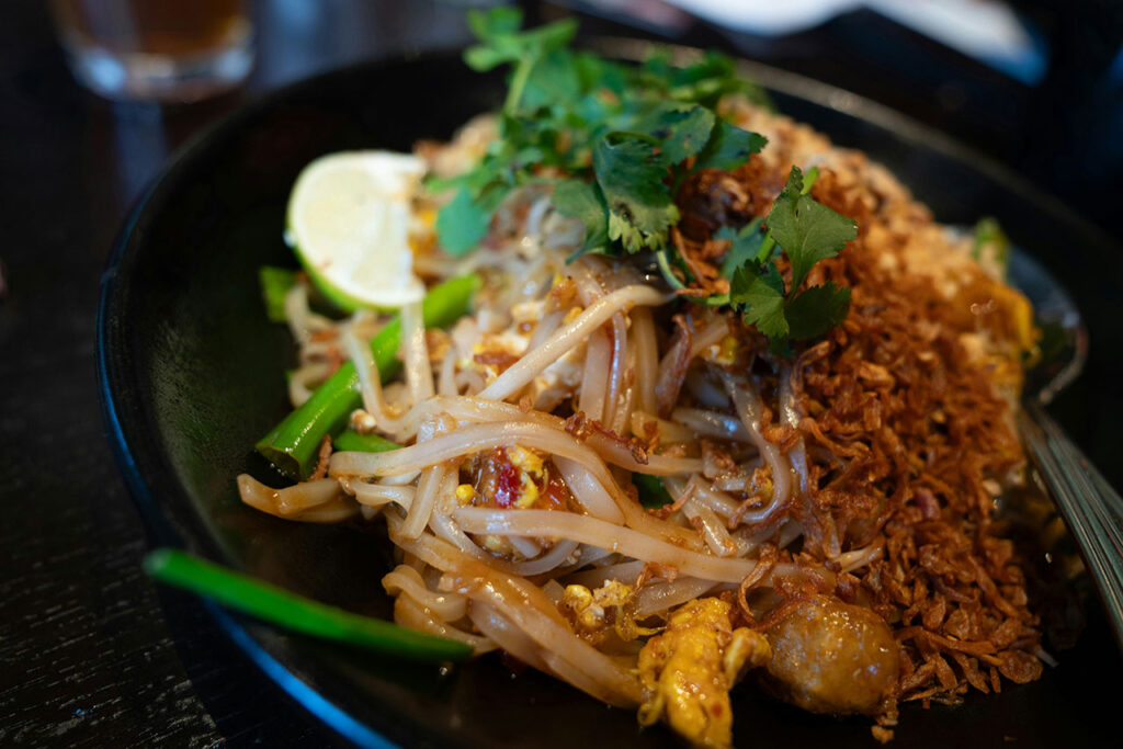 Close-up of a plate of authentic Pad Thai topped with crushed peanuts, fresh bean sprouts, cilantro, and a lime wedge.