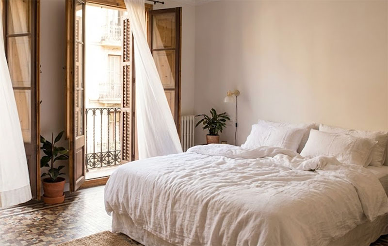 Sunlit interior of a boutique hotel room in Barcelona with tiled floors and open French doors leading to a balcony.