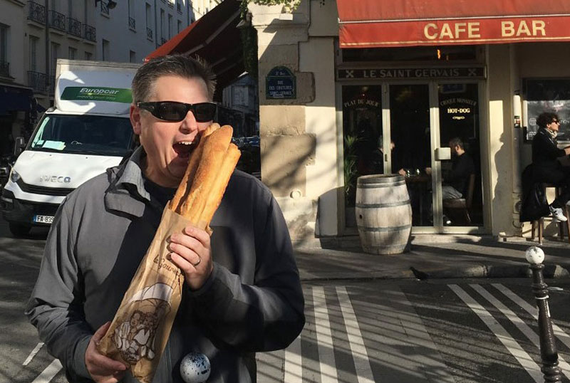 Corey Gasman eating award-winning baguettes from Tout Autour du Pain on a street corner in Le Marais, Paris.