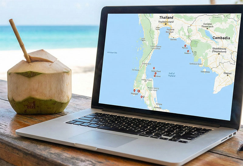 A laptop open on a table at a beachside cafe with a view of the sand.