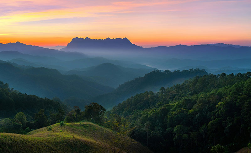 Panoramic view of layered mountain ranges in Northern Thailand during a colorful sunset with mist in the valleys.