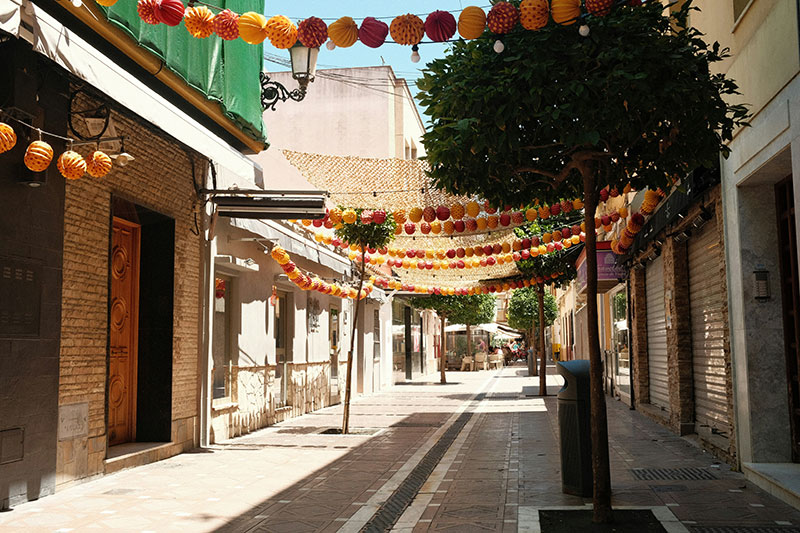 An empty Spanish street decorated with overhead garlands, presumably during siesta time.