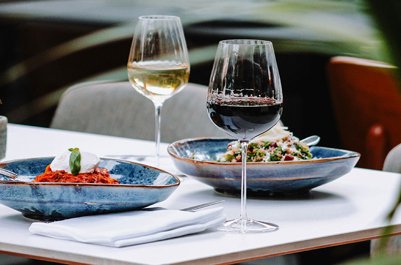 Restaurant table setting with a glass of white wine and a glass of red wine paired with plates of Italian food