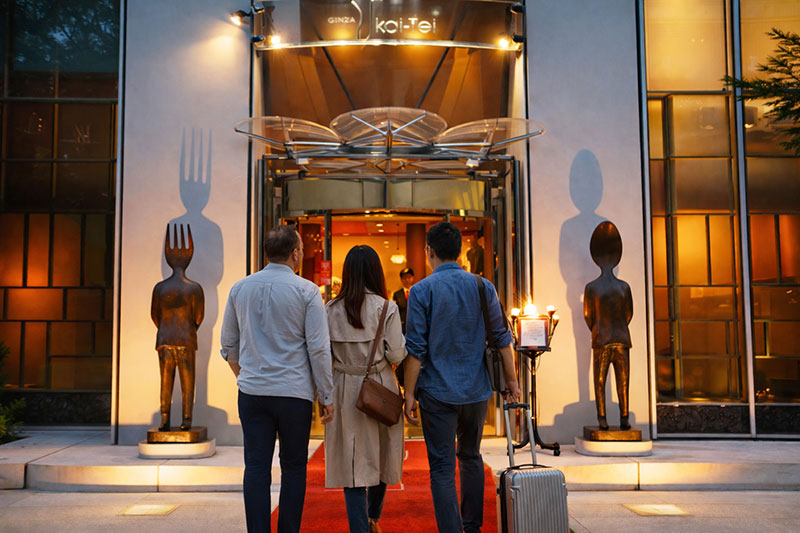 Travelers walking into the entrance of Ginza Ukai-Tei restaurant in Tokyo during the evening.