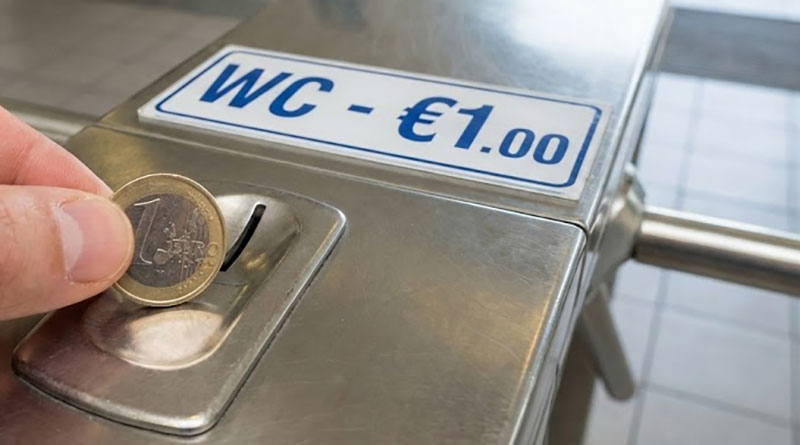 Hand inserting a one euro coin into a turnstile for a public restroom entry.