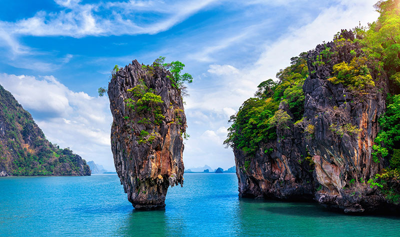 The iconic limestone karst tower of James Bond Island (Ko Ta Pu) rising out of turquoise water in Phang Nga Bay, Thailand, under a blue sky.