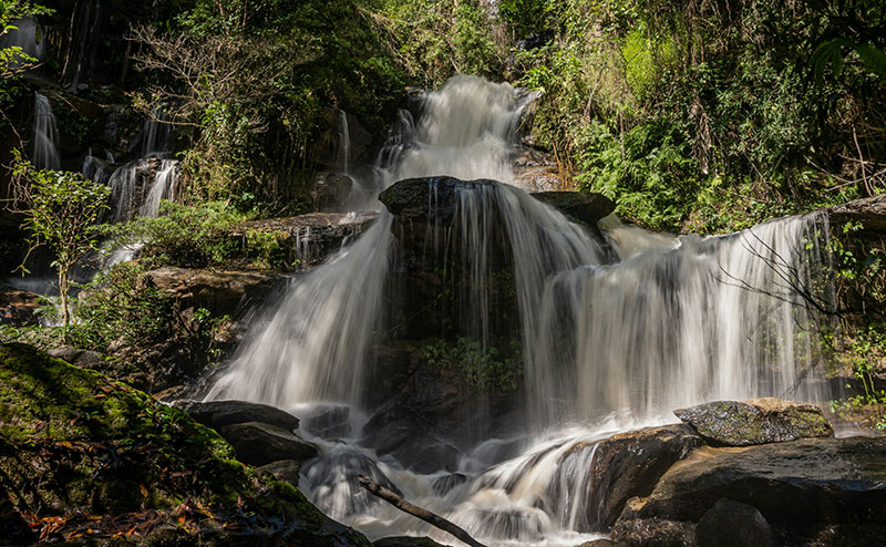 Long exposure shot of a cascading waterfall in the jungle near Chiang Mai, surrounded by green moss and trees.