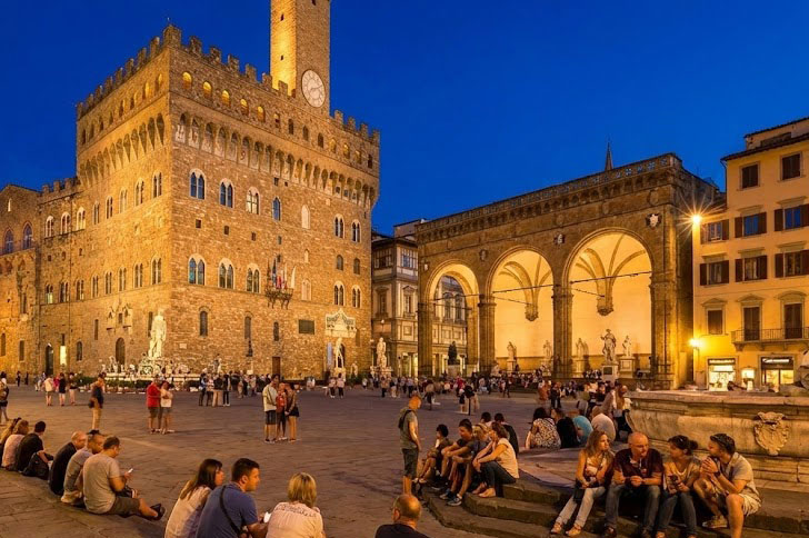 A lively and well-lit piazza in Florence at night.