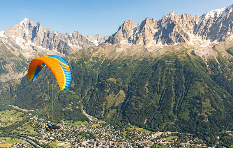 A tandem paraglider flying over the town of Chamonix with mountains in the background.