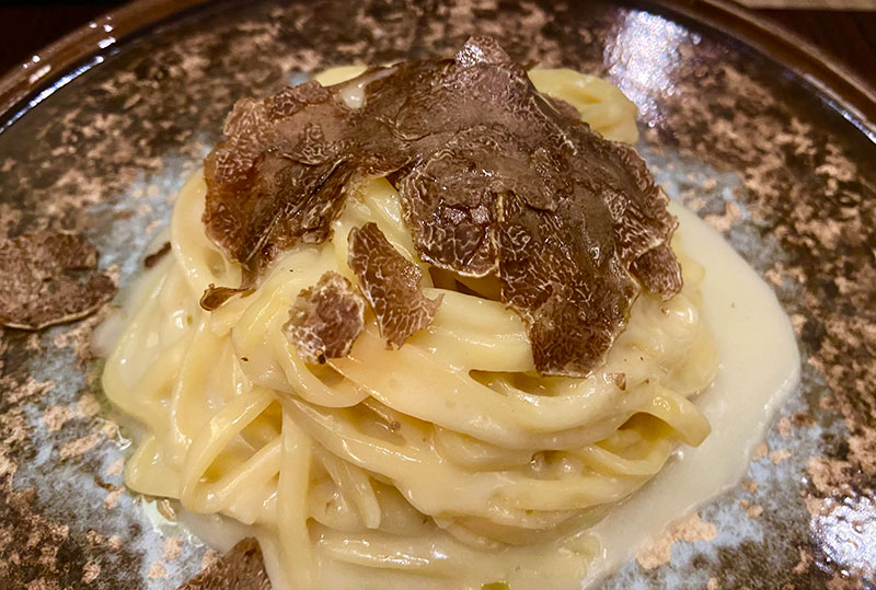 A close-up of fresh egg pasta covered in generous shavings of black truffle at a restaurant in Rome
