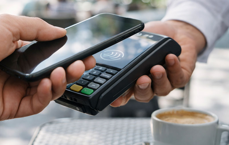 Contactless payment being made with a smartphone at a terminal in a Spanish cafe, with coffee on the table.