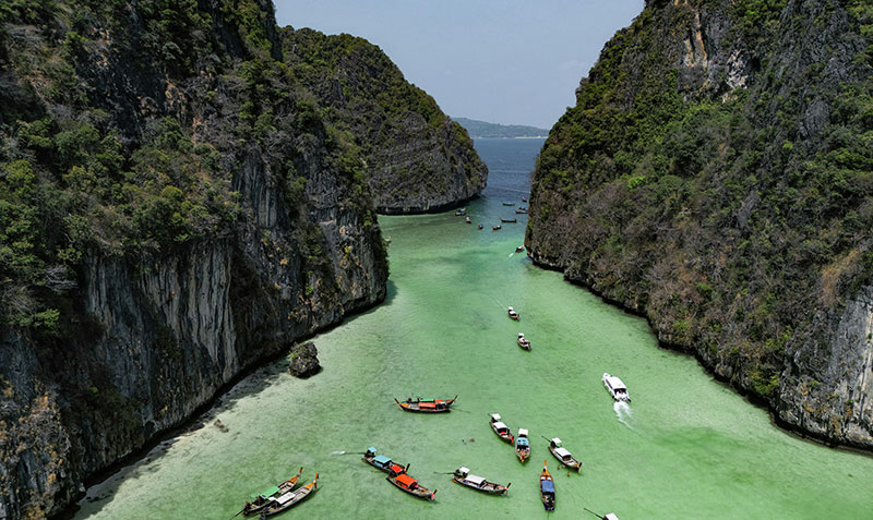 Top-down aerial view of a secluded sandy cove on Koh Tao with crystal clear emerald water and a single longtail boat.