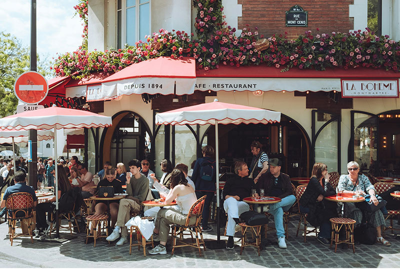 he bustling outdoor terrace of La Bohème in Montmartre, packed with customers on a sunny day, illustrating why reservations are essential for popular spots.