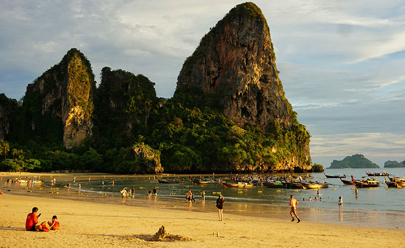 Golden hour at Railay Beach with longtail boats parked on the sand and the dramatic limestone cliffs glowing in the sunset light.