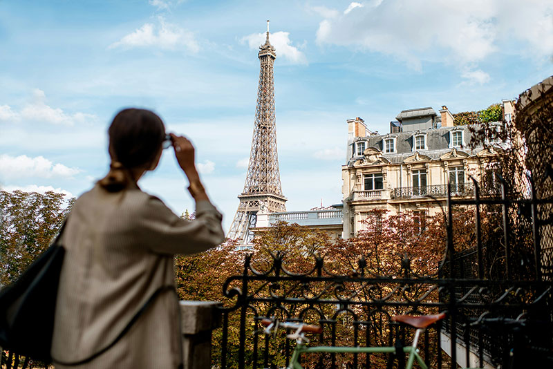 A traveler looking at the Eiffel Tower from a quiet, upscale street in the 16th Arrondissement, surrounded by classic Haussmann architecture and autumn trees.