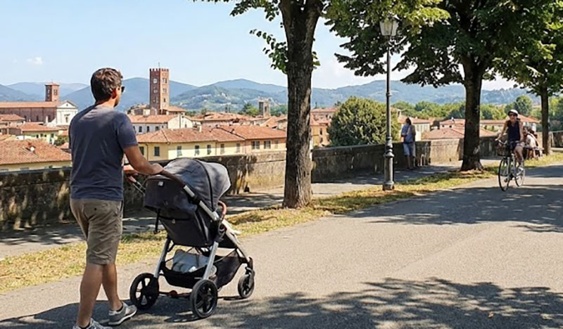 Parent pushing a stroller on the paved city walls of Lucca.