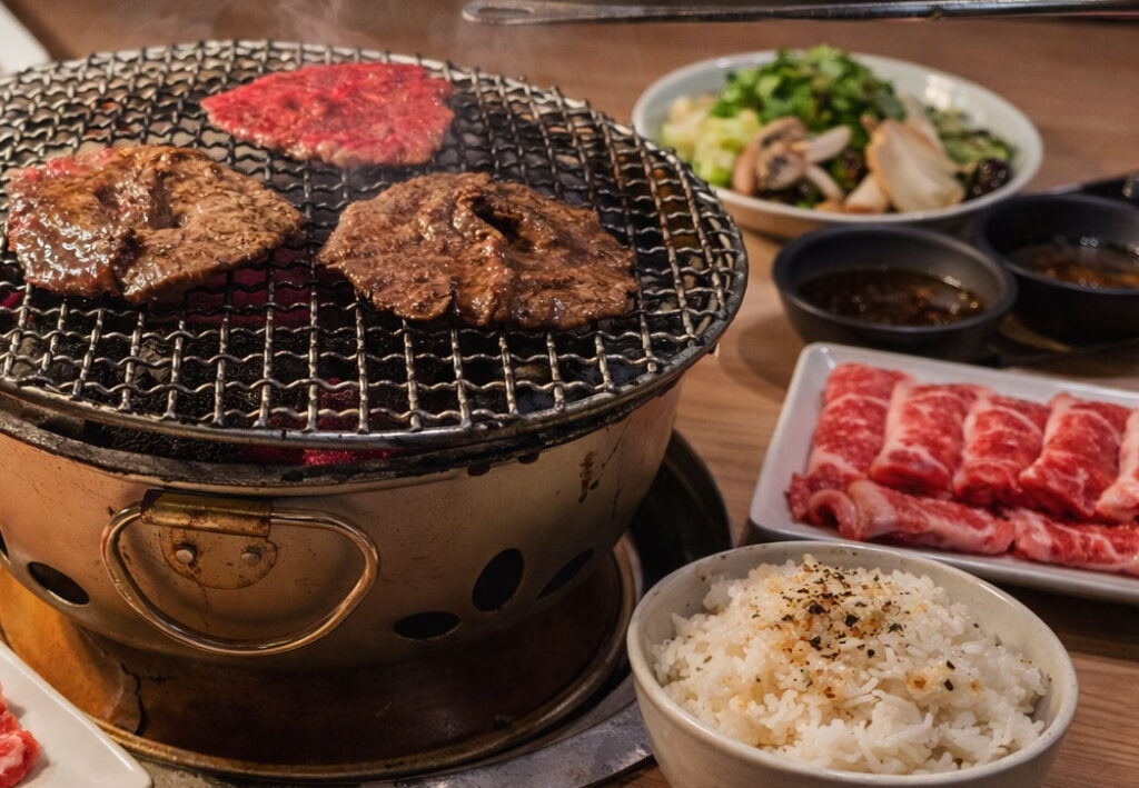 Wagyu beef grilling over charcoal at Sumibi Yakiniku Nakahara with plates of sliced beef and side dishes in Tokyo