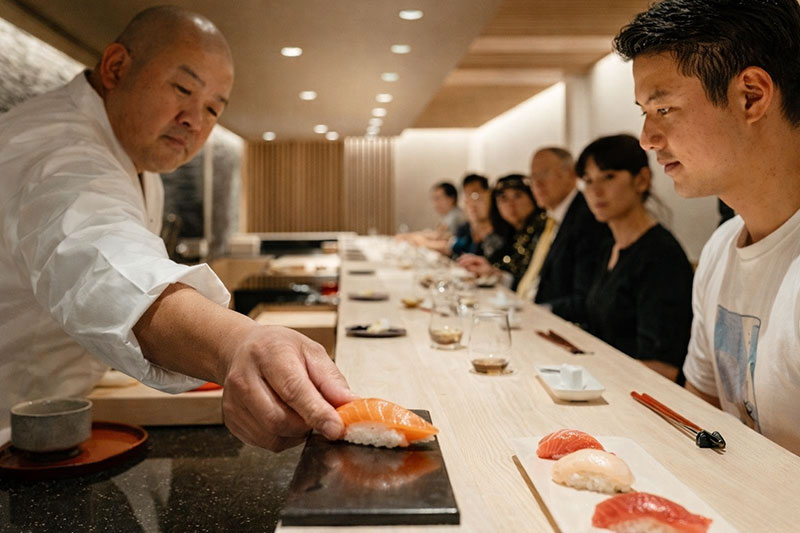 Close-up of a Japanese sushi chef placing fresh nigiri on a customer's serving plate at a high-end omakase counter in Tokyo.