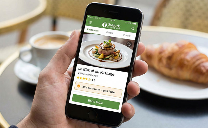 A first-person perspective of a traveler holding an iPhone displaying TheFork (La Fourchette) mobile app to make a restaurant reservation in Paris.