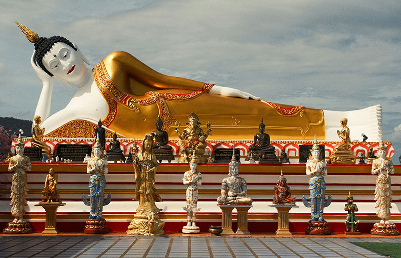 Reclining Buddha statue at Wat Phra That Doi Kham in Chiang Mai, Thailand, featuring white skin and gold robes surrounded by smaller shrines.