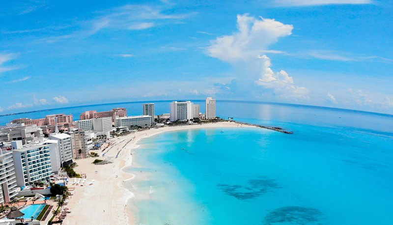 Aerial view of the turquoise Caribbean Sea and white sand beaches along the Cancun Hotel Zone coastline with high-rise resorts. Caption: The iconic turquoise waters and luxury resorts of the Cancun Hotel Zone.