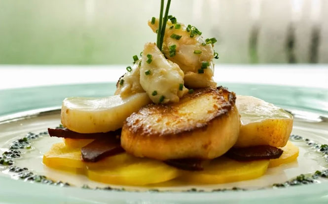 A close-up of a gourmet seafood dish from Commander's Palace, featuring tender sautéed shrimp and seared scallops served over a bed of creamy stone-ground grits with a rich Creole meunière sauce.