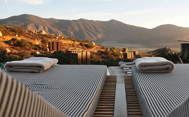 A modern rooftop lounge area at Encuentro Guadalupe with minimalist furniture, overlooking the vast valley and rugged mountains of Valle de Guadalupe.