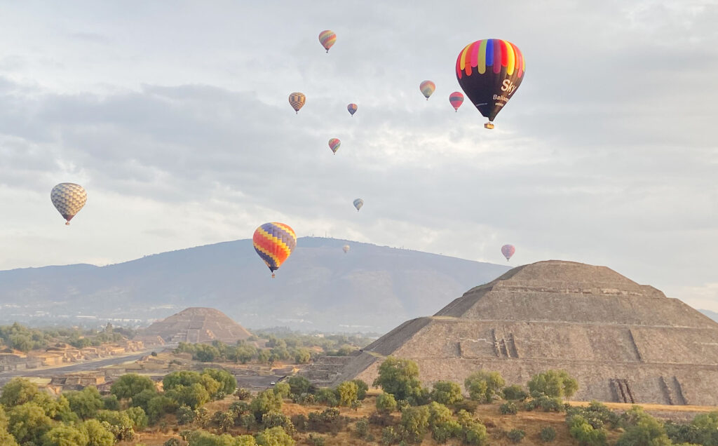 A cinematic sunrise view of colorful hot air balloons floating over the ancient stone pyramids of Teotihuacán near Mexico City.