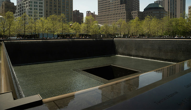 An elevated view of one of the twin reflecting pools at the National September 11 Memorial & Museum, showing the recessed waterfall and the bronze parapets engraved with names of the victims.