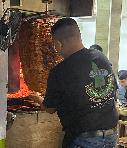 Chef slicing Al Pastor meat from the vertical spit (trompo) at Pancho's Takos.