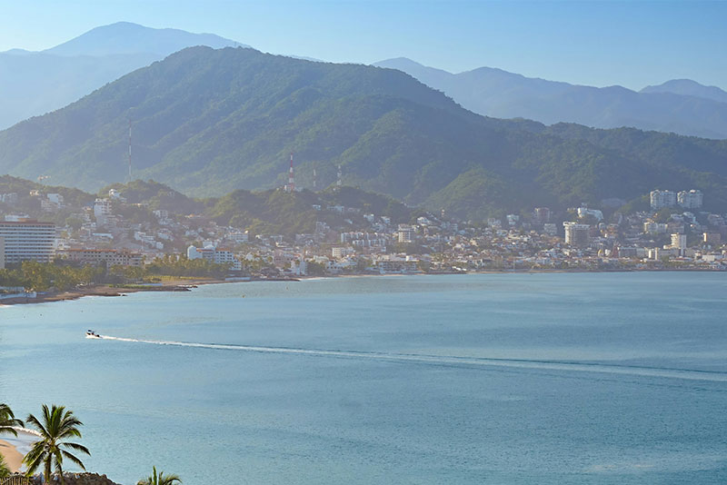 Scenic aerial view of the Banderas Bay coastline in Puerto Vallarta, featuring golden sand beaches, luxury oceanfront resorts, and the Sierra Madre mountains in the background.