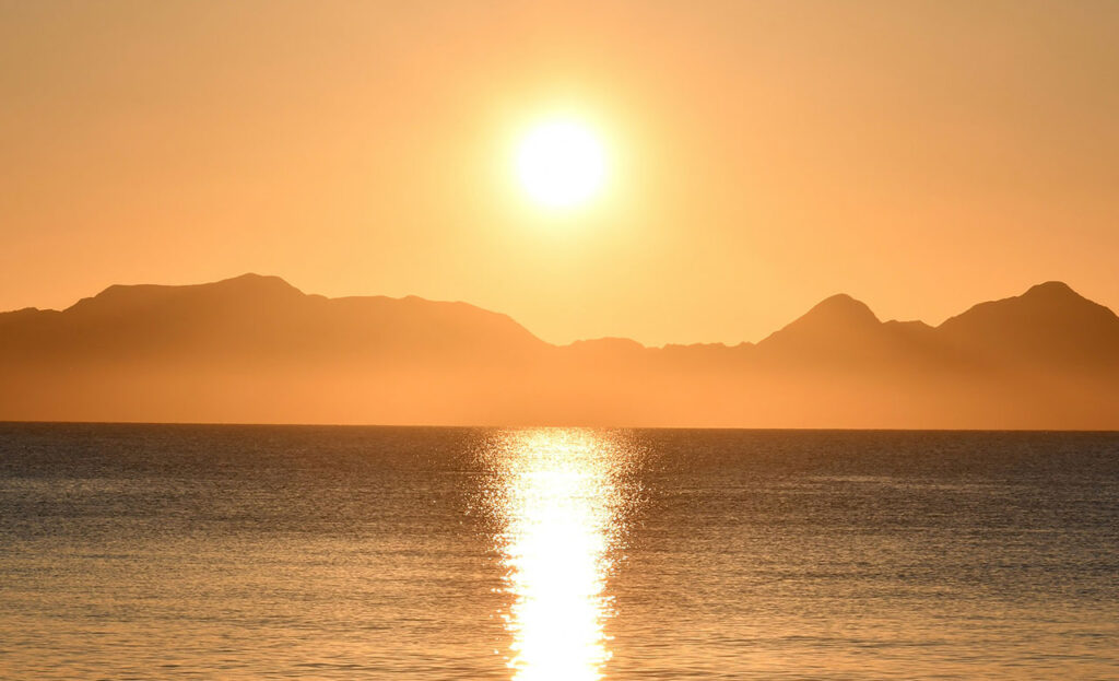 A breathtaking sunrise over the calm waters of Loreto, Baja California Sur, with the silhouette of the rugged Sierra de la Giganta mountains and the offshore islands in the distance.