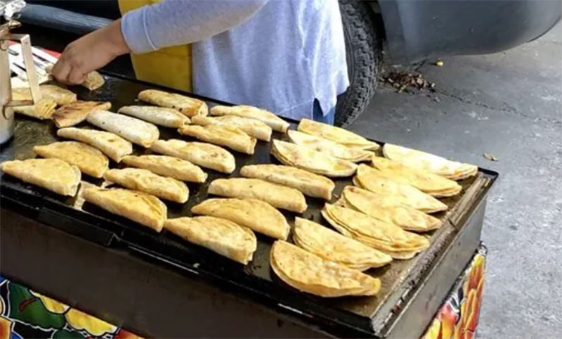 Rows of golden tacos de birria crisping on the flat-top griddle at the Tacos de Birria Chanfay street stand.