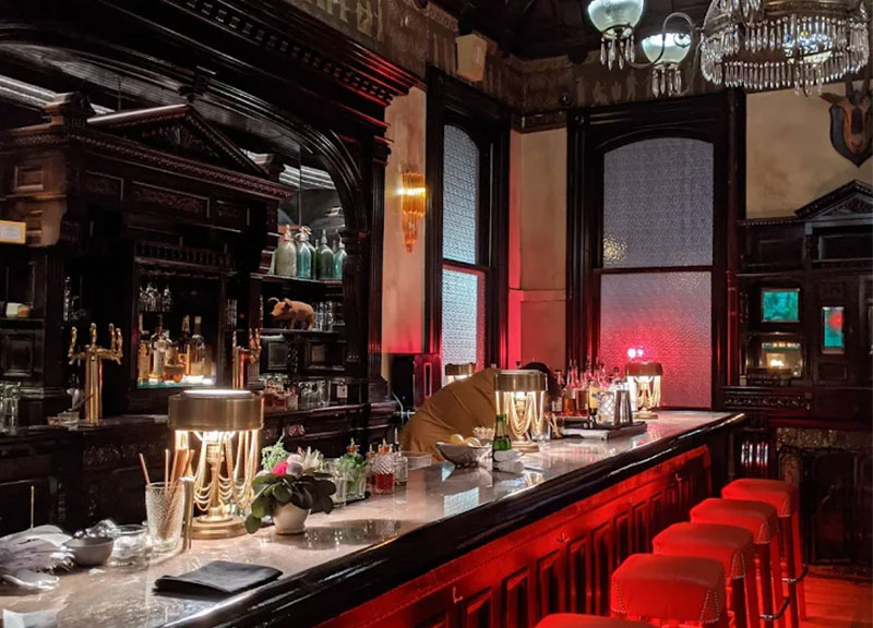 A view of the elegant, historic interior of The Columns on St. Charles Avenue, featuring tall windows, dark wood accents, and a classic bar area that overlooks the Garden District.