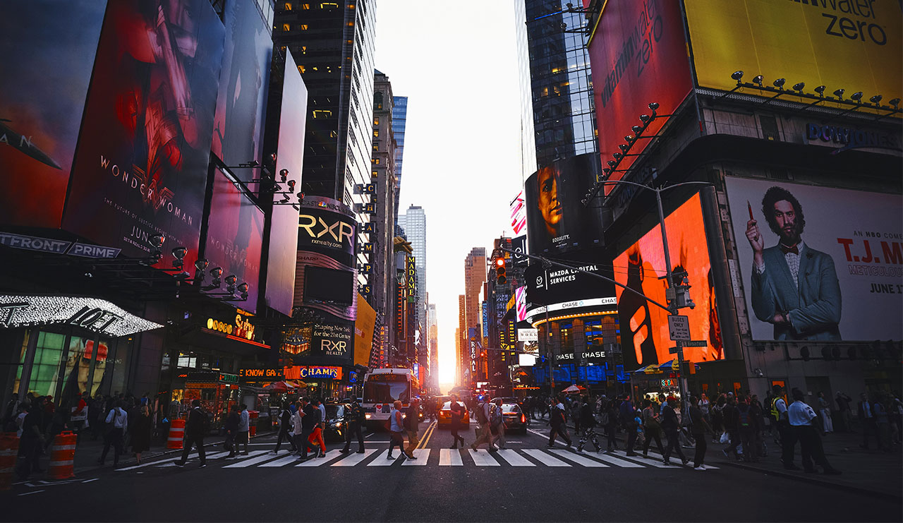 A high-energy, nighttime view of Times Square in New York City, featuring glowing digital billboards, bright neon advertisements, and the bustling atmosphere of the iconic intersection.