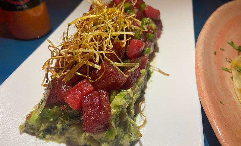Close-up of tuna montaditos appetizer with avocado, diced tuna, and crispy fried onions on top.