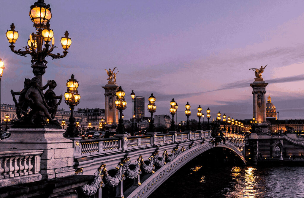 The ornate Pont Alexandre III bridge in Paris at dusk, featuring its golden statues and classic lamp posts over the Seine River.