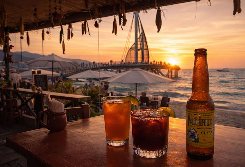 Sunset at Cuates y Cuetes in Puerto Vallarta with beach tables, ocean views, and drinks on a table near the Malecón.